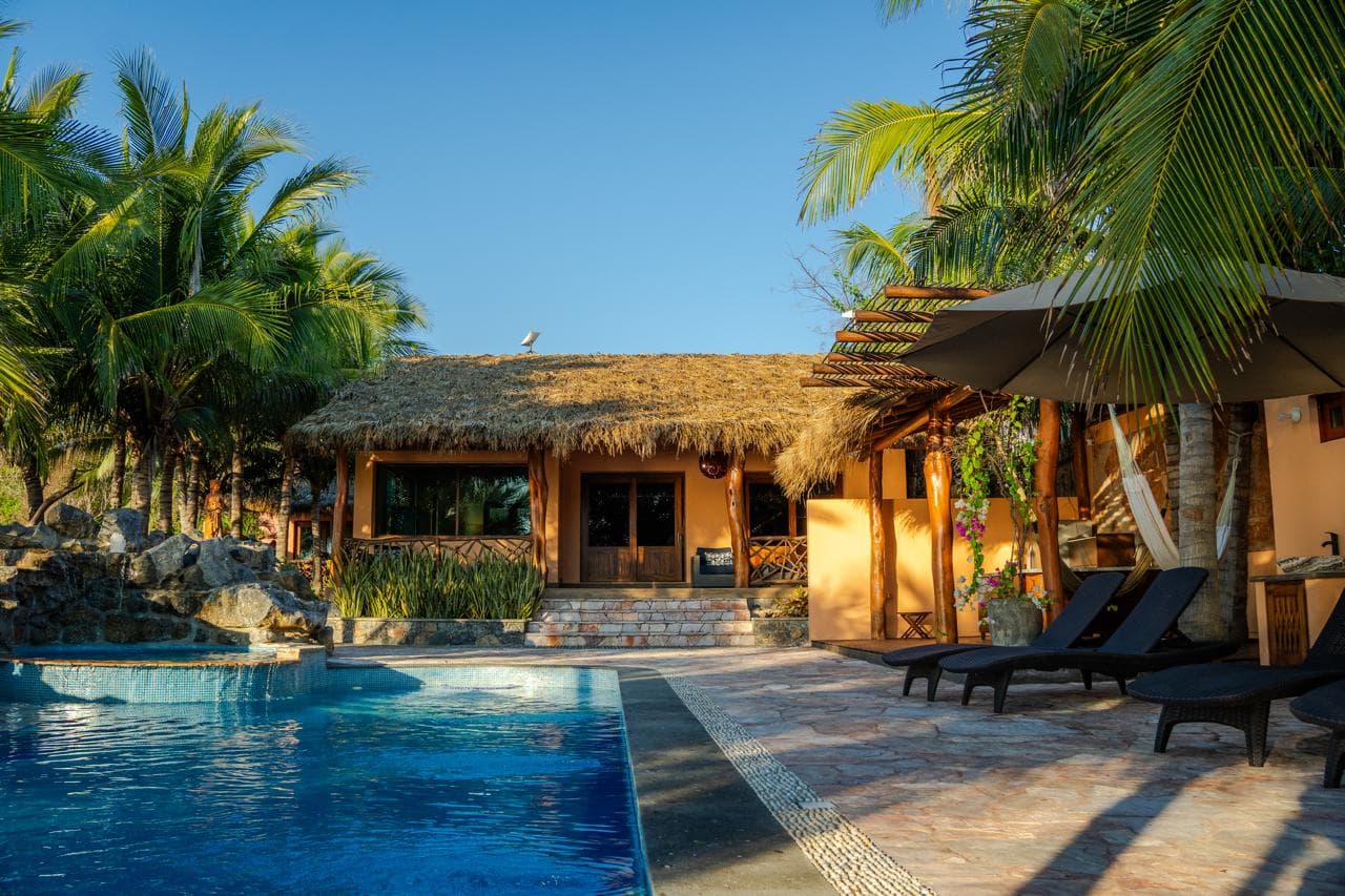 Villa au toit de palme et chaises longues sur la terrasse de pierre au bord de la piscine